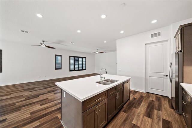 kitchen featuring dark wood-type flooring, dark brown cabinetry, sink, appliances with stainless steel finishes, and an island with sink