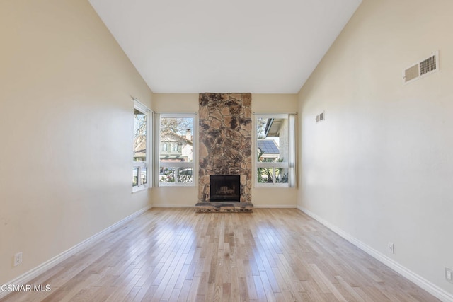 unfurnished living room featuring a stone fireplace, high vaulted ceiling, and light hardwood / wood-style floors