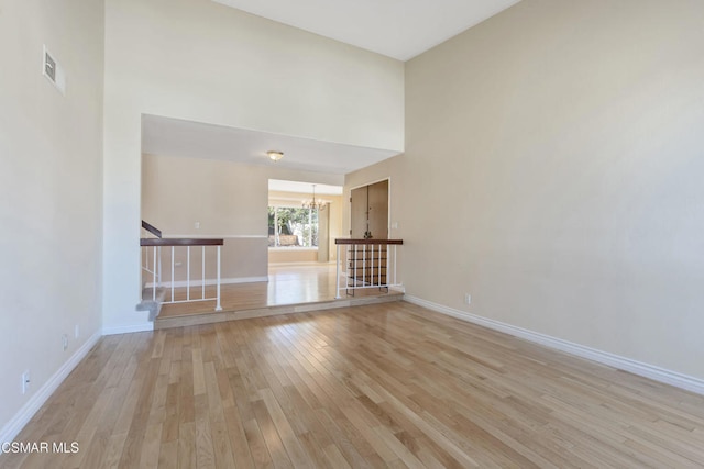 unfurnished living room with a high ceiling, light wood-type flooring, and an inviting chandelier