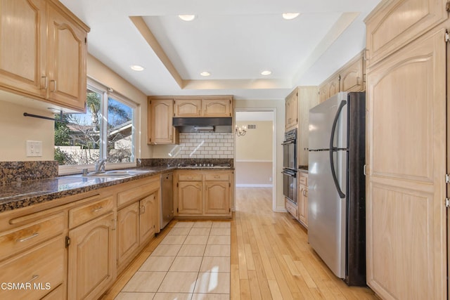 kitchen featuring light brown cabinetry, black appliances, sink, dark stone counters, and a tray ceiling