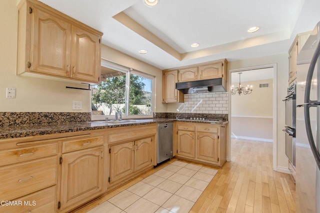 kitchen with sink, dark stone countertops, light brown cabinetry, and a tray ceiling