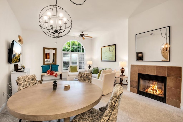 dining room with ceiling fan with notable chandelier, a tiled fireplace, and carpet floors