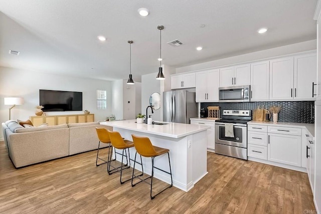 kitchen with sink, appliances with stainless steel finishes, hanging light fixtures, an island with sink, and white cabinets