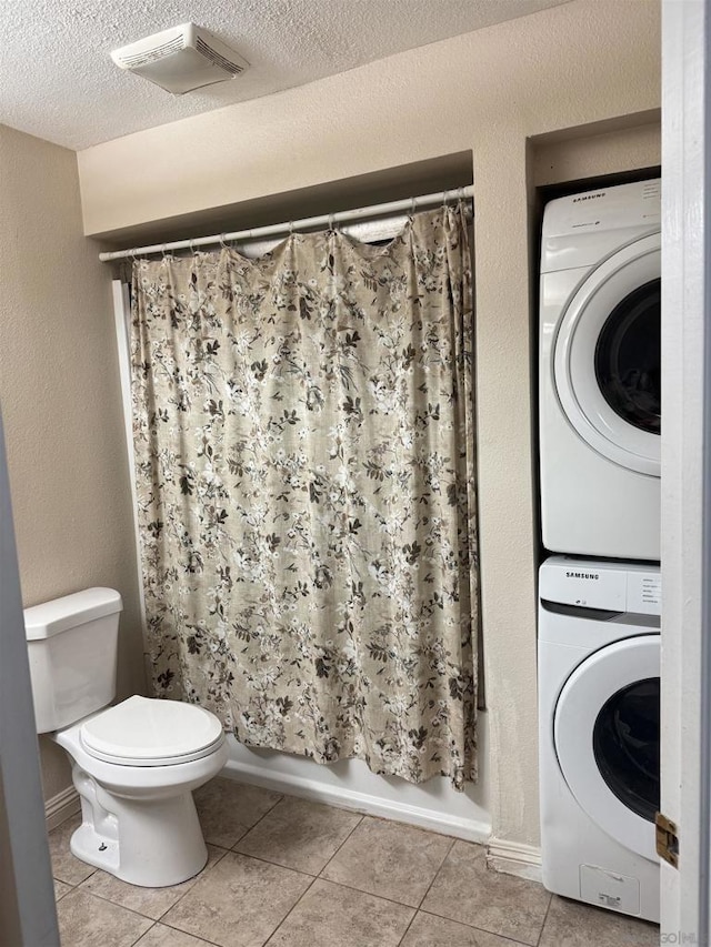 interior space with tile patterned floors, stacked washer and clothes dryer, toilet, and a textured ceiling