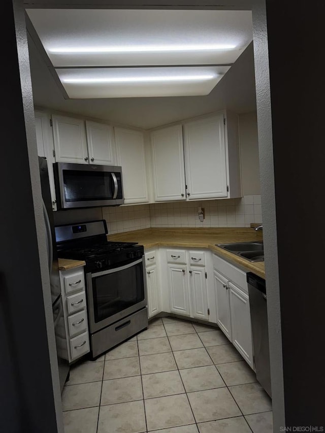 kitchen featuring tasteful backsplash, sink, white cabinets, light tile patterned floors, and stainless steel appliances