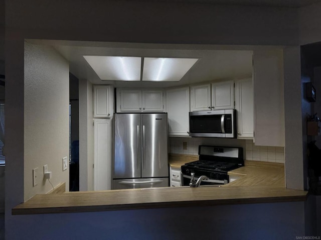 kitchen with white cabinetry, appliances with stainless steel finishes, kitchen peninsula, and decorative backsplash