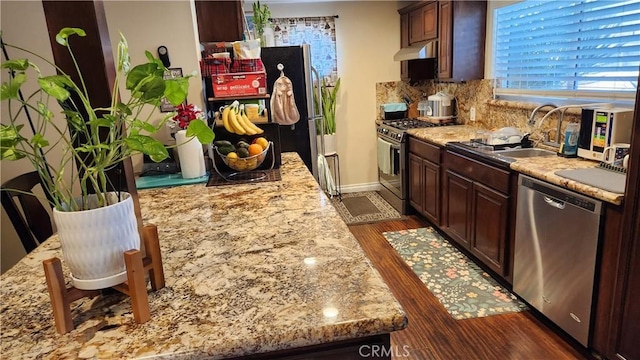 kitchen with tasteful backsplash, sink, dark hardwood / wood-style flooring, light stone counters, and stainless steel appliances