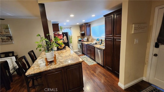 kitchen with dark brown cabinets, appliances with stainless steel finishes, dark hardwood / wood-style floors, a kitchen breakfast bar, and light stone countertops