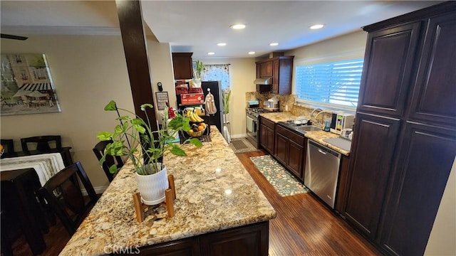 kitchen with appliances with stainless steel finishes, backsplash, a center island, dark hardwood / wood-style floors, and light stone countertops