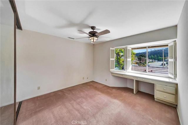 interior space featuring ceiling fan, light colored carpet, and built in desk