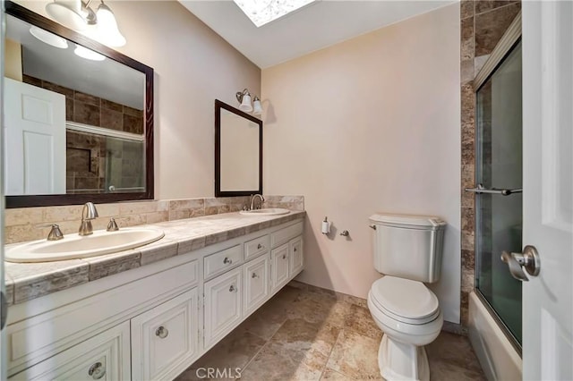 full bathroom with a skylight, vanity, combined bath / shower with glass door, and toilet