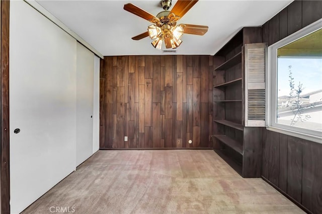 carpeted empty room with ceiling fan and wooden walls