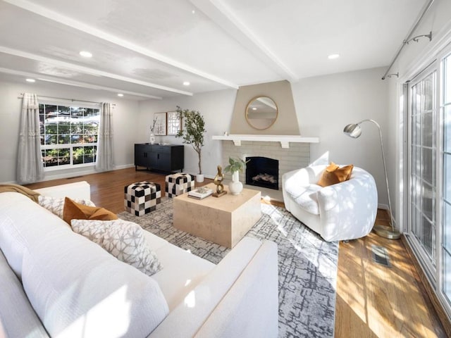 living room featuring beamed ceiling, hardwood / wood-style floors, and a brick fireplace