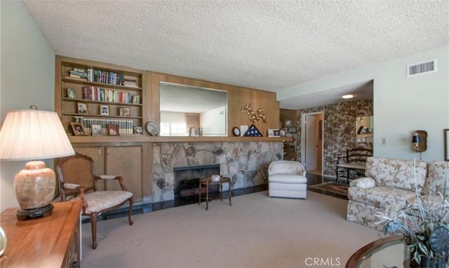 sitting room with a stone fireplace, carpet flooring, built in features, and a textured ceiling