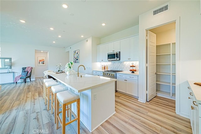 kitchen featuring stainless steel appliances, an island with sink, and white cabinetry