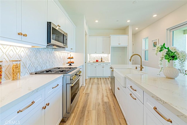 kitchen with sink, stainless steel appliances, white cabinets, and light stone countertops