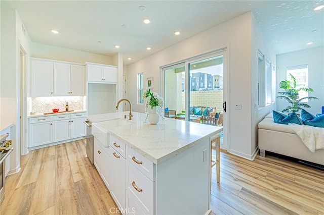 kitchen featuring sink, white cabinetry, light stone counters, light hardwood / wood-style flooring, and an island with sink