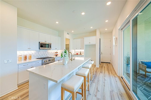 kitchen with a breakfast bar area, appliances with stainless steel finishes, white cabinetry, light stone countertops, and a center island with sink