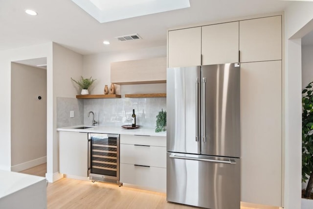 interior space featuring tasteful backsplash, sink, wine cooler, high end fridge, and light hardwood / wood-style flooring