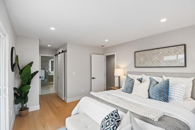 bedroom featuring ensuite bath, a barn door, and light wood-type flooring