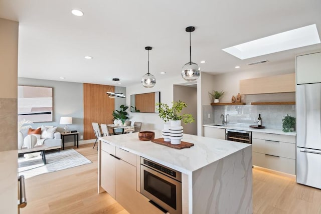 kitchen featuring built in fridge, a kitchen island, a skylight, wine cooler, and light wood-type flooring