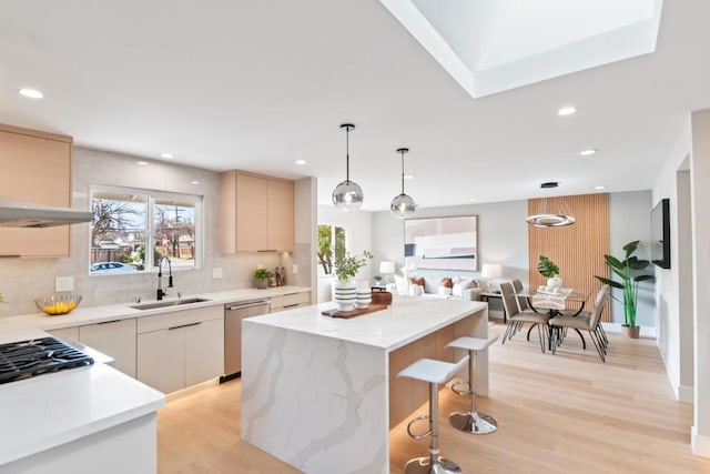 kitchen with sink, decorative light fixtures, a center island, dishwasher, and light stone countertops