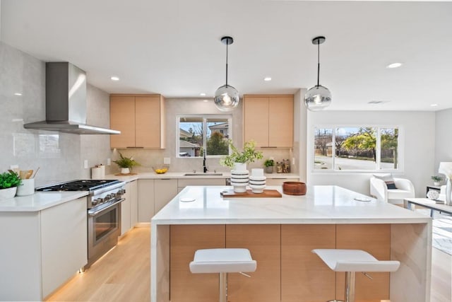 kitchen featuring pendant lighting, wall chimney range hood, sink, stainless steel range, and light brown cabinetry