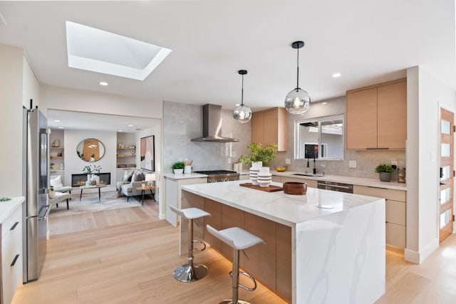 kitchen featuring wall chimney exhaust hood, sink, a kitchen island, pendant lighting, and stainless steel appliances