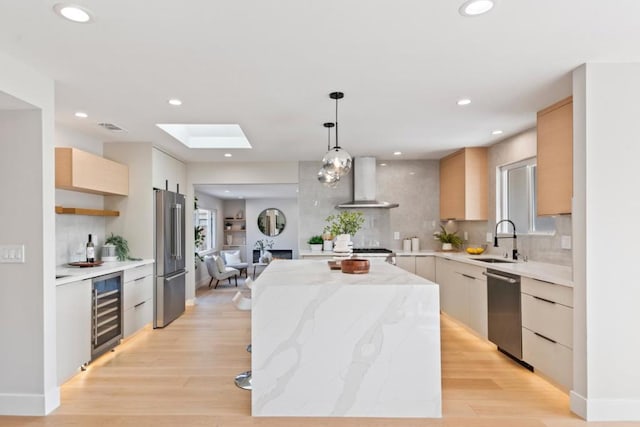 kitchen with a kitchen island, sink, beverage cooler, hanging light fixtures, and wall chimney range hood