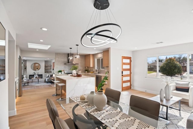 dining space with a chandelier, a skylight, sink, and light wood-type flooring