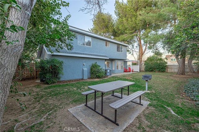 rear view of house featuring stucco siding, a lawn, central AC unit, a patio area, and a fenced backyard