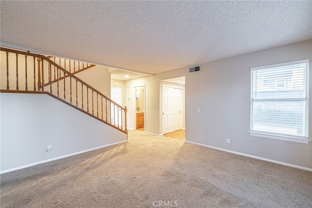 spare room featuring baseboards, visible vents, light colored carpet, stairs, and a textured ceiling