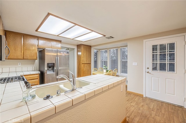 kitchen with light wood finished floors, visible vents, tile counters, appliances with stainless steel finishes, and brown cabinets