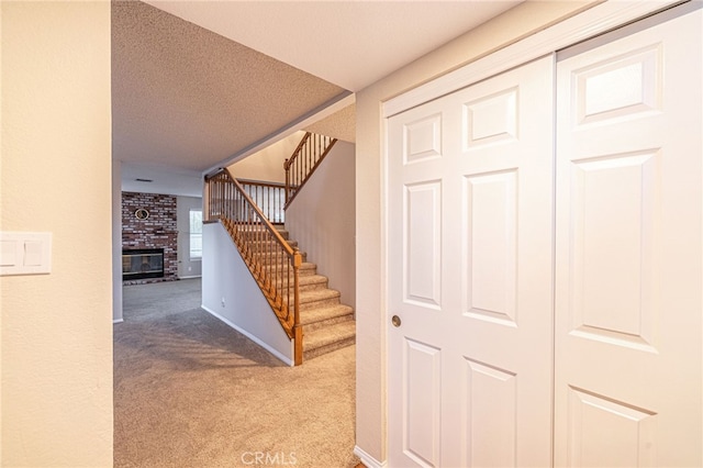 stairs with a textured ceiling, a brick fireplace, carpet flooring, and baseboards