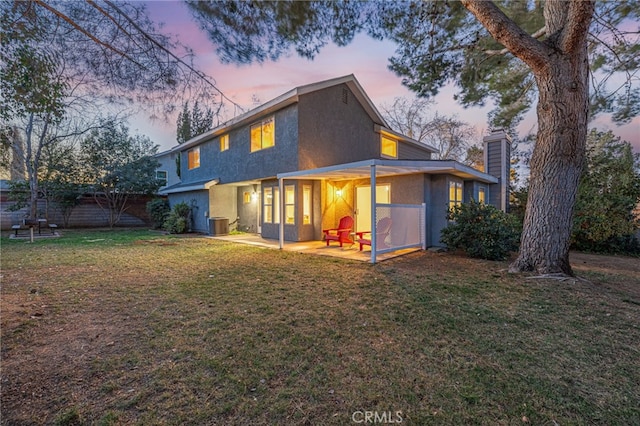 back of property at dusk with a lawn, a patio area, fence, and stucco siding