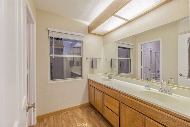 bathroom with double vanity, baseboards, a sink, and wood finished floors