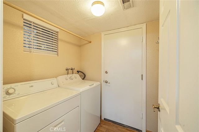 laundry room featuring washing machine and clothes dryer, visible vents, a textured ceiling, wood finished floors, and laundry area