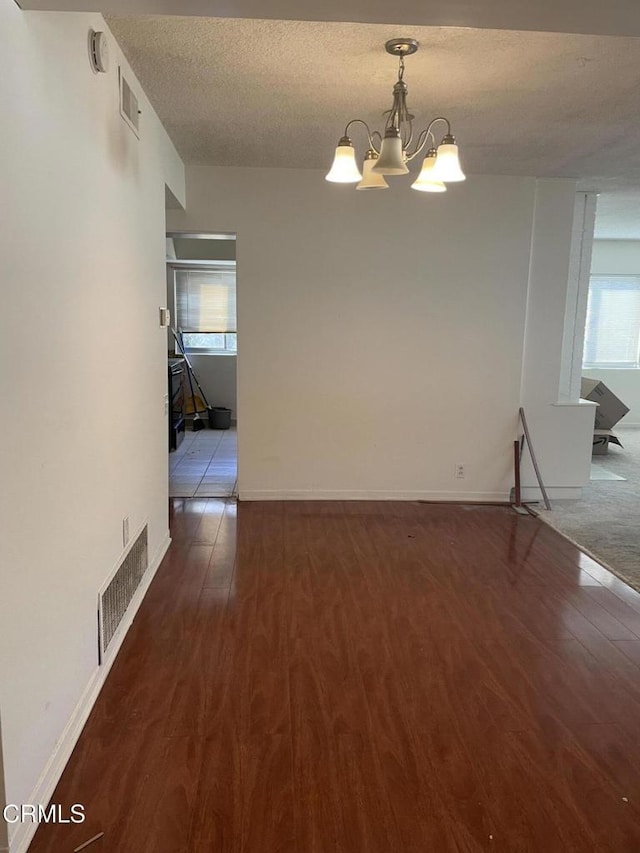 spare room featuring a notable chandelier, dark hardwood / wood-style floors, and a textured ceiling