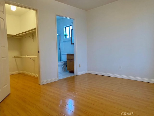 unfurnished bedroom featuring a spacious closet, baseboards, a closet, and light wood-type flooring