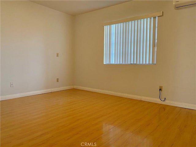 unfurnished room with baseboards, light wood-style flooring, and an AC wall unit