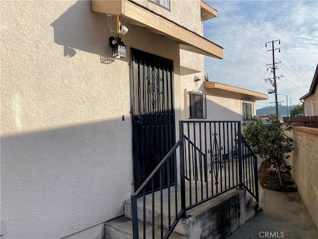 doorway to property featuring fence and stucco siding
