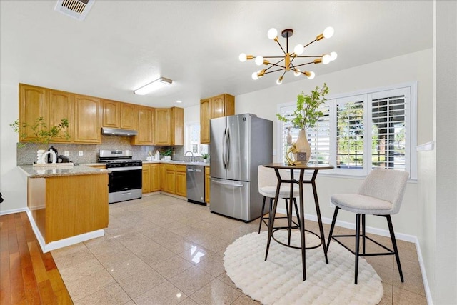 kitchen with appliances with stainless steel finishes, tasteful backsplash, sink, a chandelier, and light stone counters