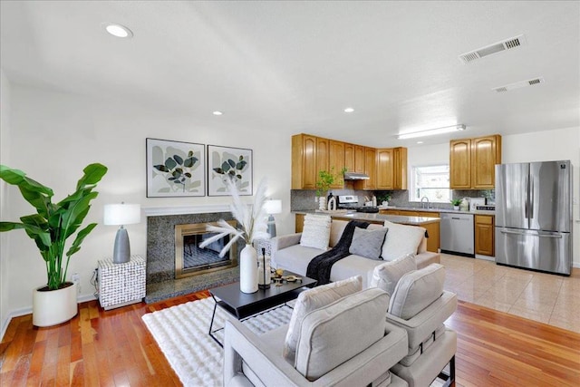 living room featuring a high end fireplace, sink, and light hardwood / wood-style flooring