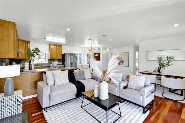 living room with dark wood-type flooring, an inviting chandelier, and sink