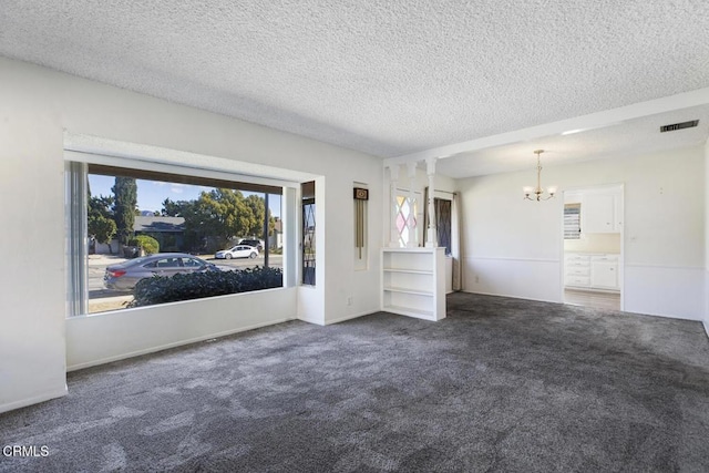 spare room featuring dark colored carpet, a textured ceiling, and an inviting chandelier