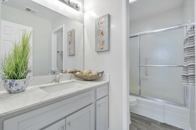 full bathroom with vanity, hardwood / wood-style floors, enclosed tub / shower combo, and toilet