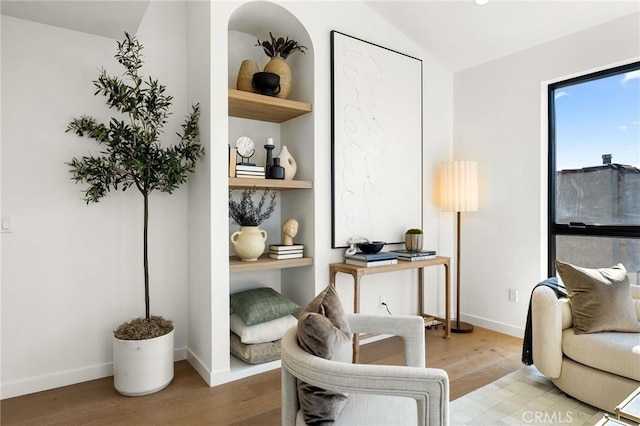 sitting room with built in features, baseboards, vaulted ceiling, and wood finished floors