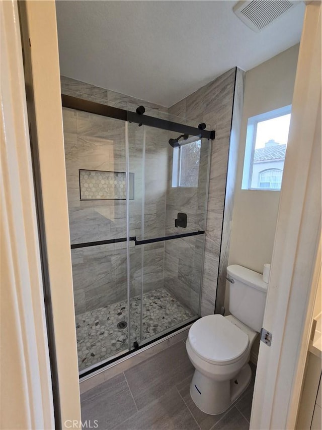 bathroom featuring a shower with shower door, tile patterned floors, and toilet