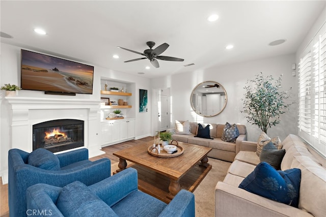 living room with built in features, light hardwood / wood-style floors, and ceiling fan