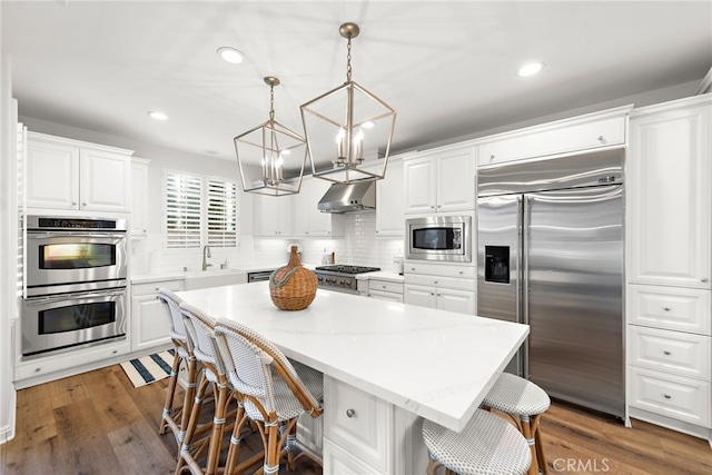 kitchen with white cabinetry, hanging light fixtures, a center island, built in appliances, and tasteful backsplash